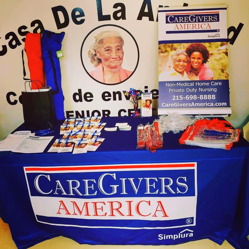 Indoor display table promoting CareGivers America with banners and brochures.
