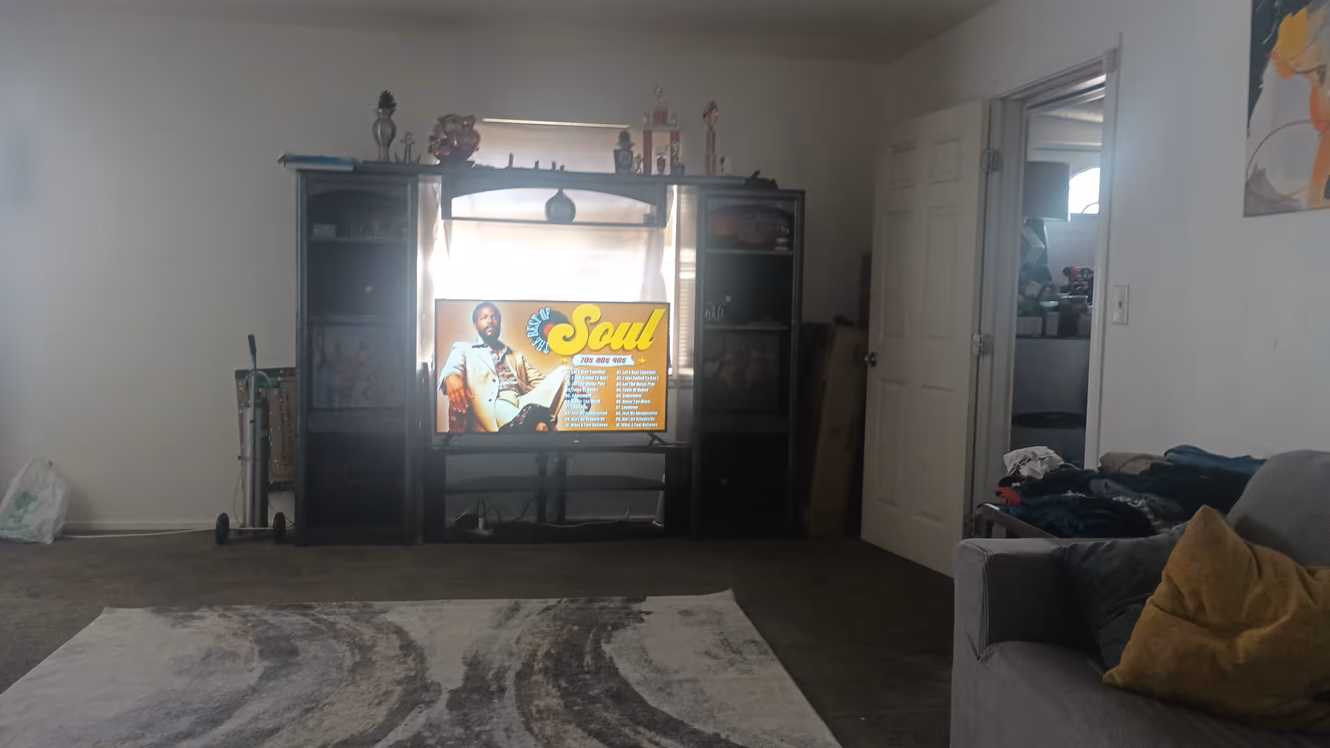 A living room with a TV stand, couch, rug, and cluttered doorway.