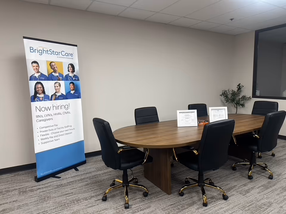 A BrightStar Care conference room with an oval table, black chairs, and a hiring banner.