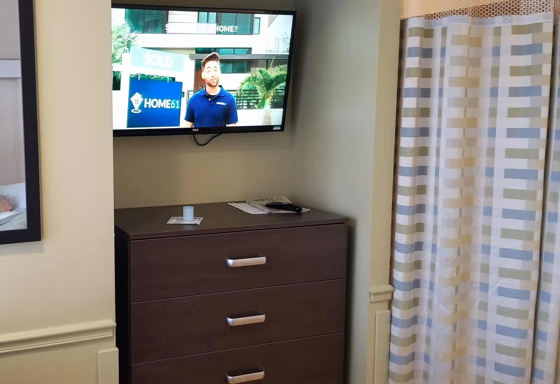 A dresser with a wall-mounted TV sits in a bedroom with striped curtains.
