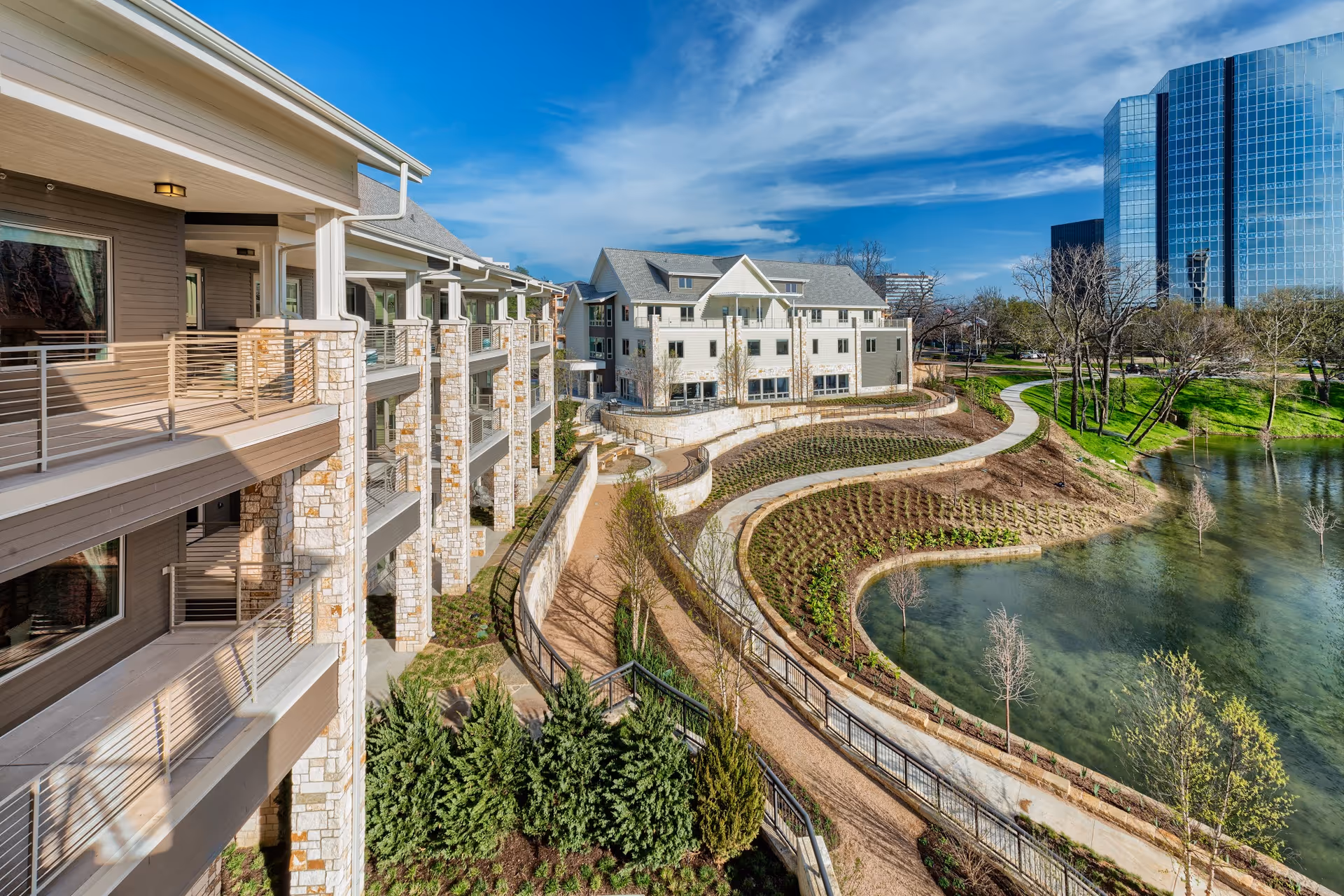 Outdoor view of a senior living campus with stone balconies, winding paths, and a pond.