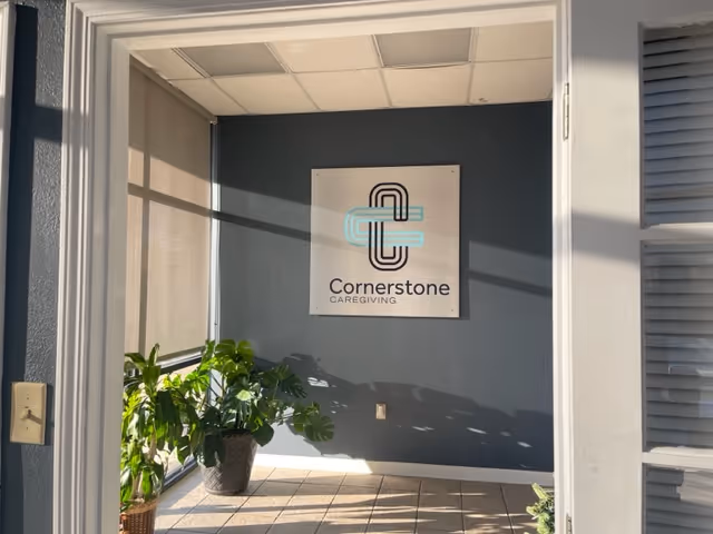 Indoor entryway with a Cornerstone Caregiving sign on a blue wall and potted plants.