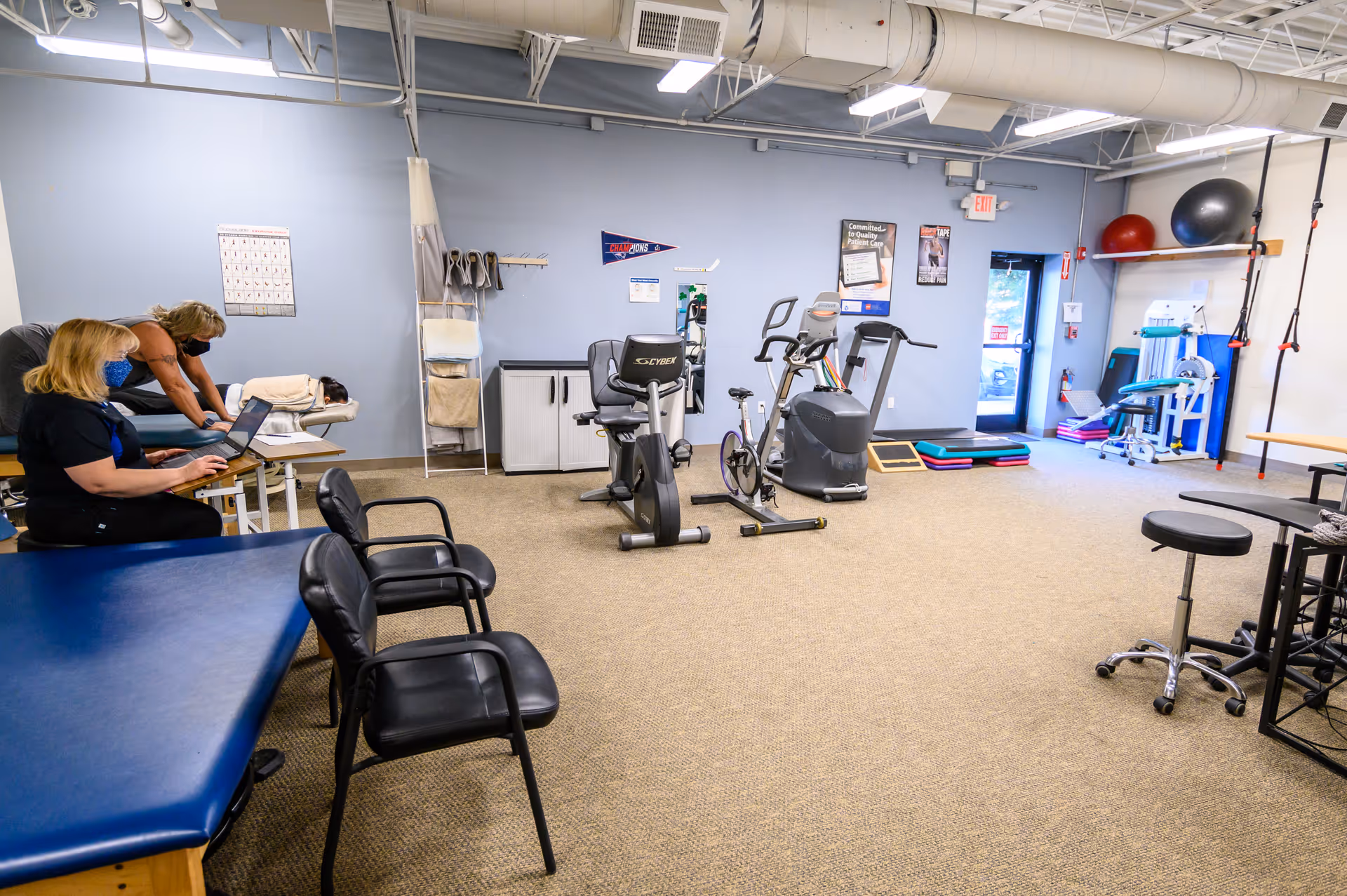 A spacious interior physical therapy room with exercise bikes, mats, and a treatment table.