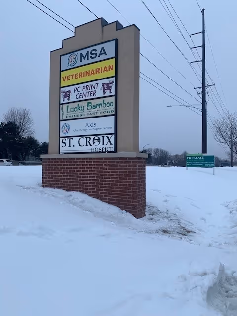 Tall stone sign displays St. Croix Hospice and other tenants in a snowy parking lot.