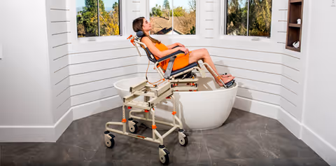 Person in orange sits on a medical chair in a bright white bathroom showroom.