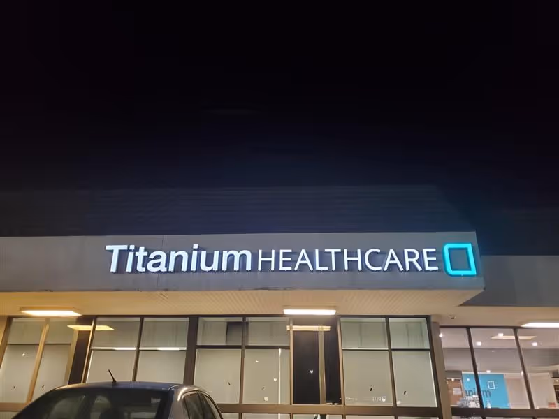 Exterior view of Titanium Healthcare storefront at night with illuminated sign and glass windows.