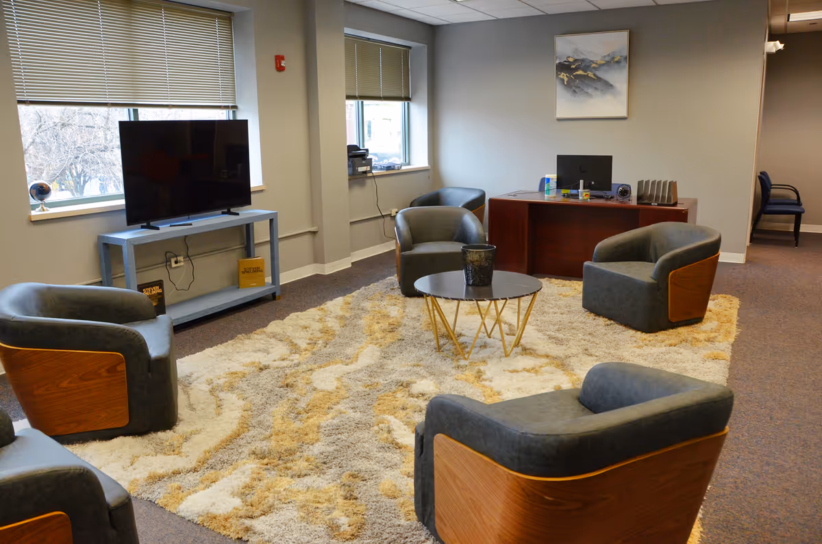 A modern lounge with gray chairs around a round coffee table on a shag rug.