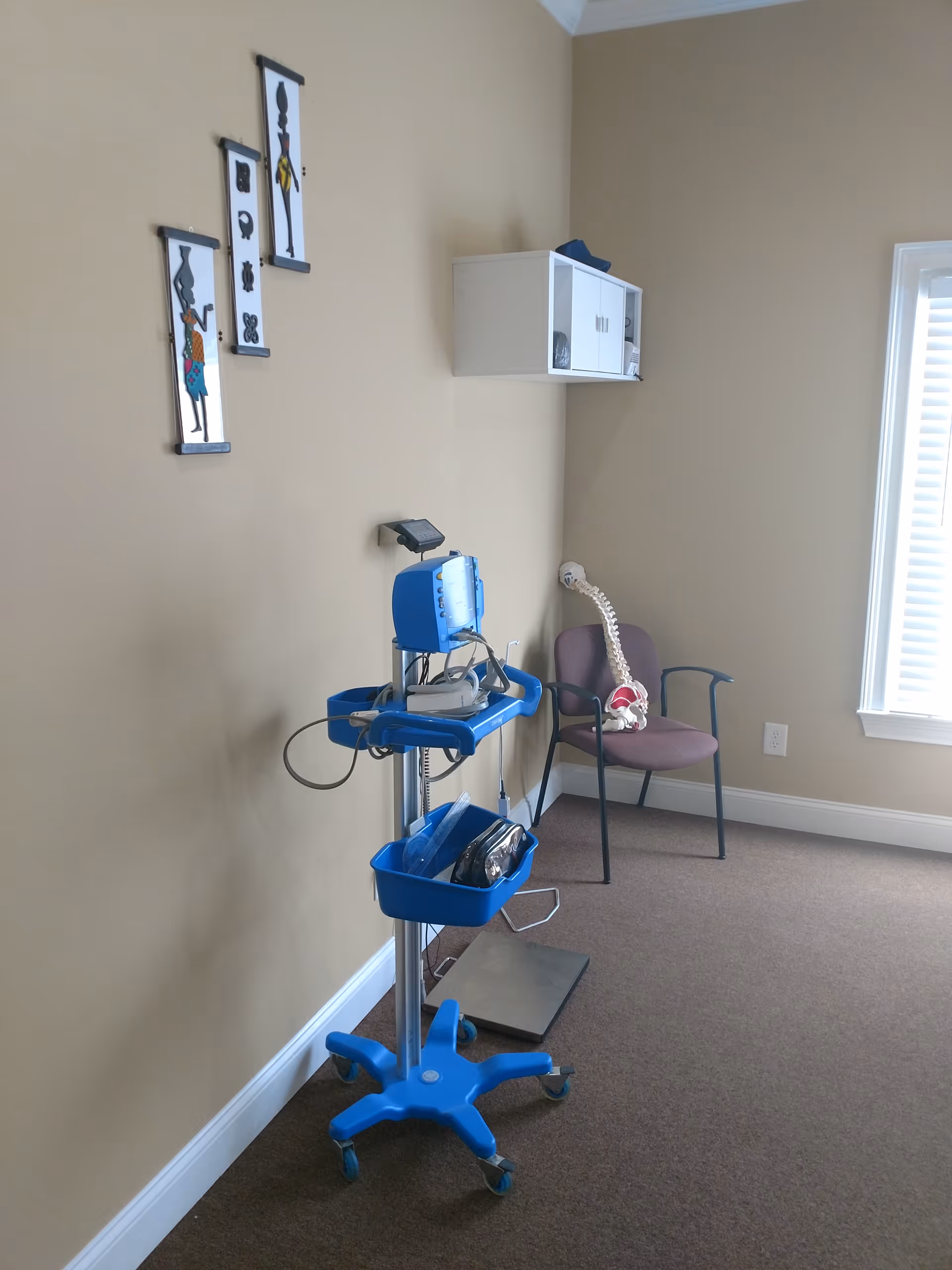 Blue medical cart with monitoring device stands in beige clinic room corner.