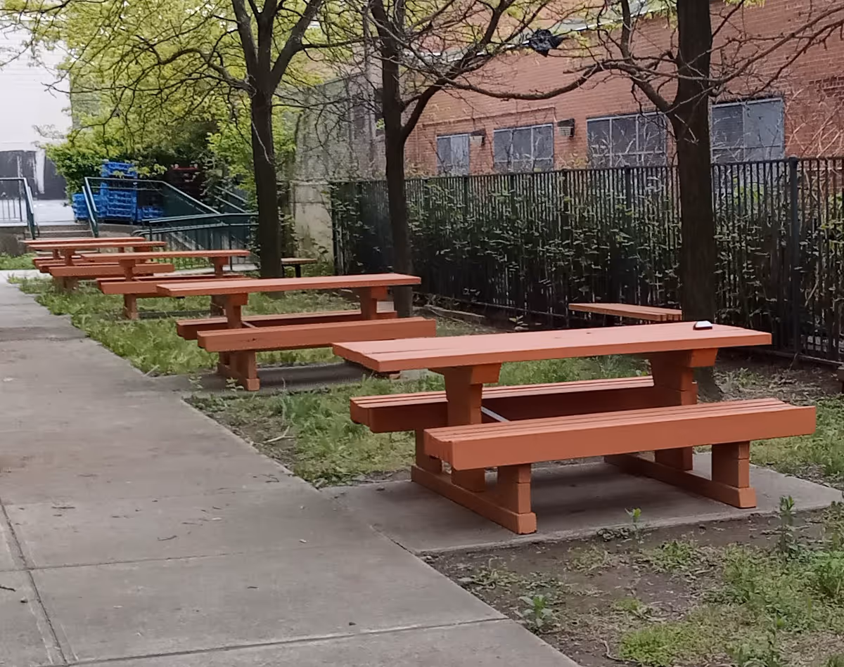 Outdoor walkway with orange picnic tables and trees beside a brick building.