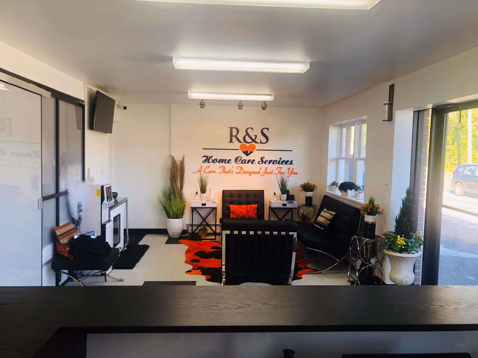 Interior lobby showing R&S Home Care Services sign, seating area, plants, and windows.