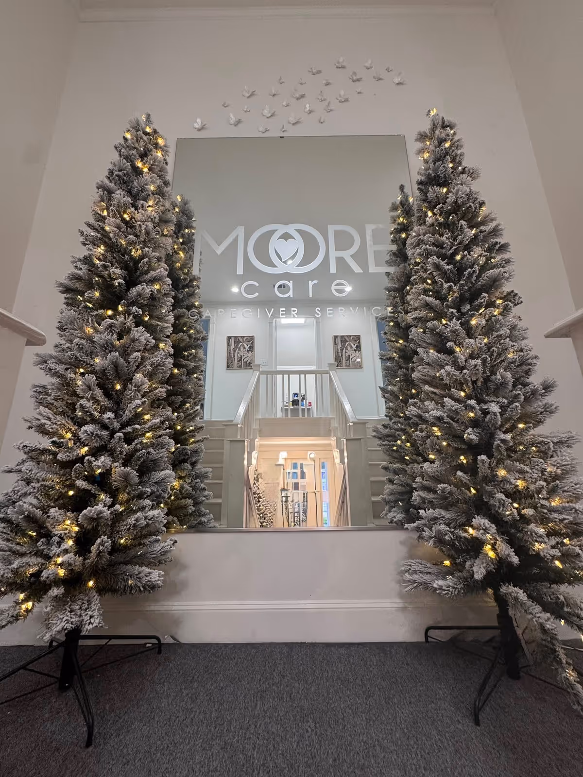 Indoor lobby with snow-dusted Christmas trees, a large mirror, and a staircase reflection.