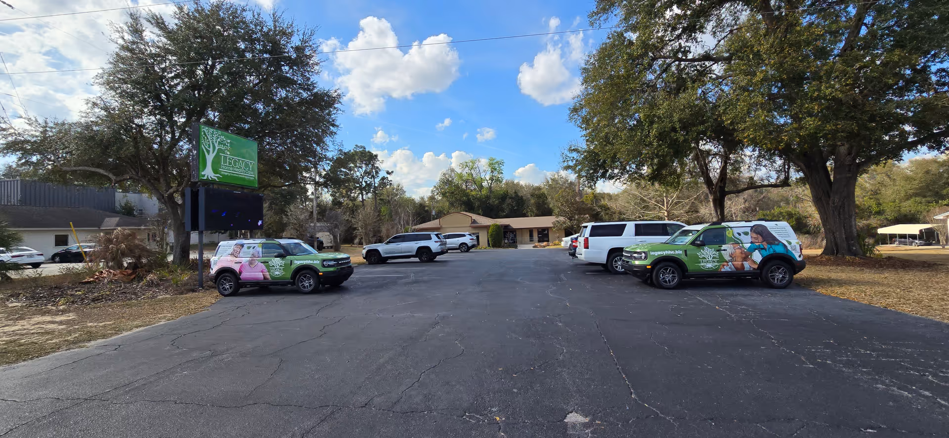 Parking lot view outside Legacy Home Health Care with branded vans and trees.