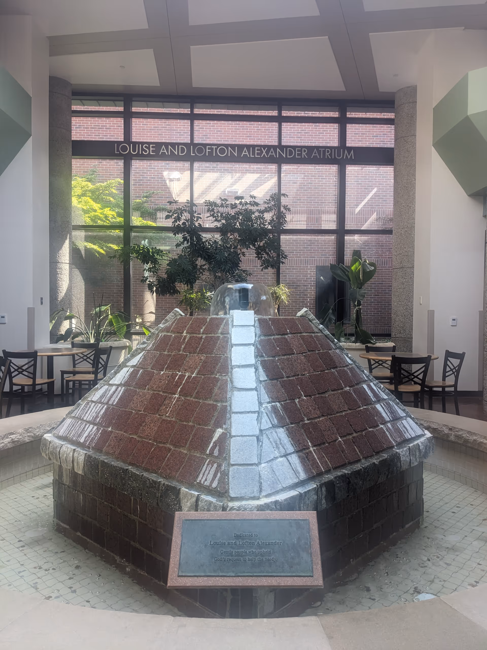 Indoor atrium featuring a large pyramid fountain, seating, plants, and glass walls.