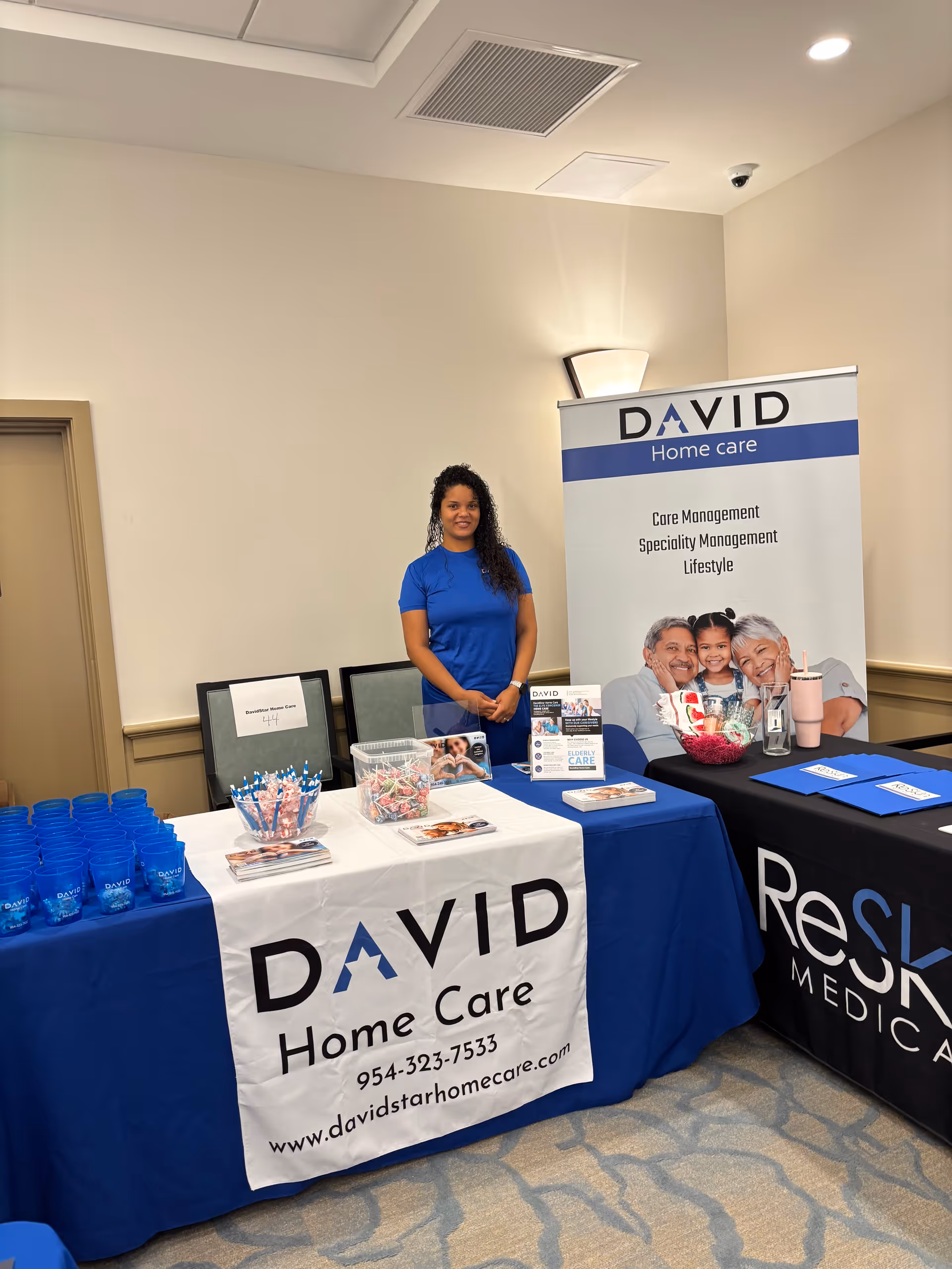 A staff member stands beside a David Home Care information booth inside a facility.