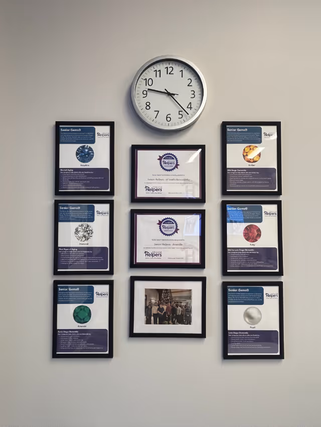 Wall display featuring a large round clock and multiple framed certificates, with a central group photo.