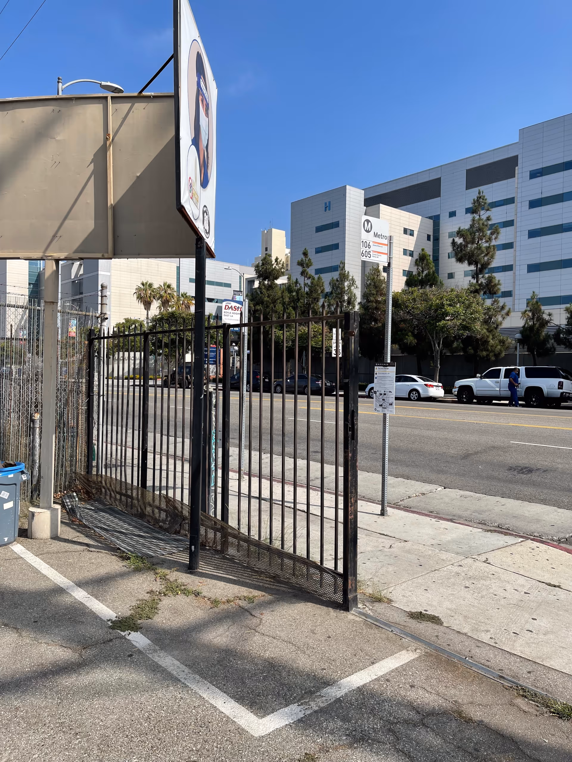 Metal gate blocks a sidewalk in front of a large, modern hospital-like building.