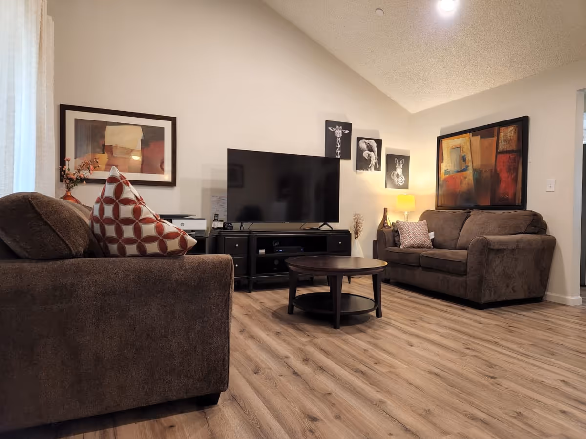 Cozy living room with brown sofas, a TV, artwork, and a round coffee table.