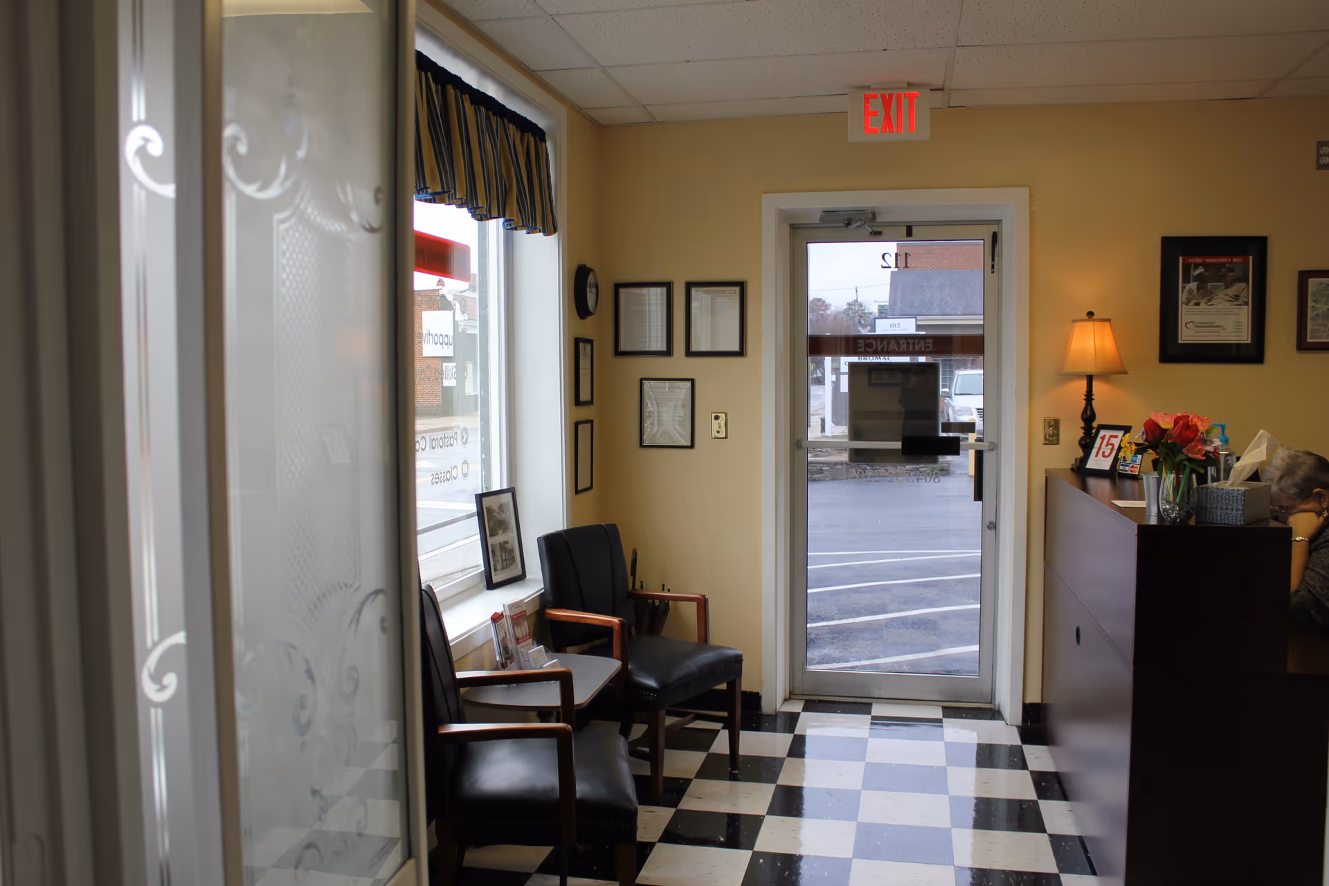 Lobby area with checkered floor, chairs, reception desk, and glass door to outside.