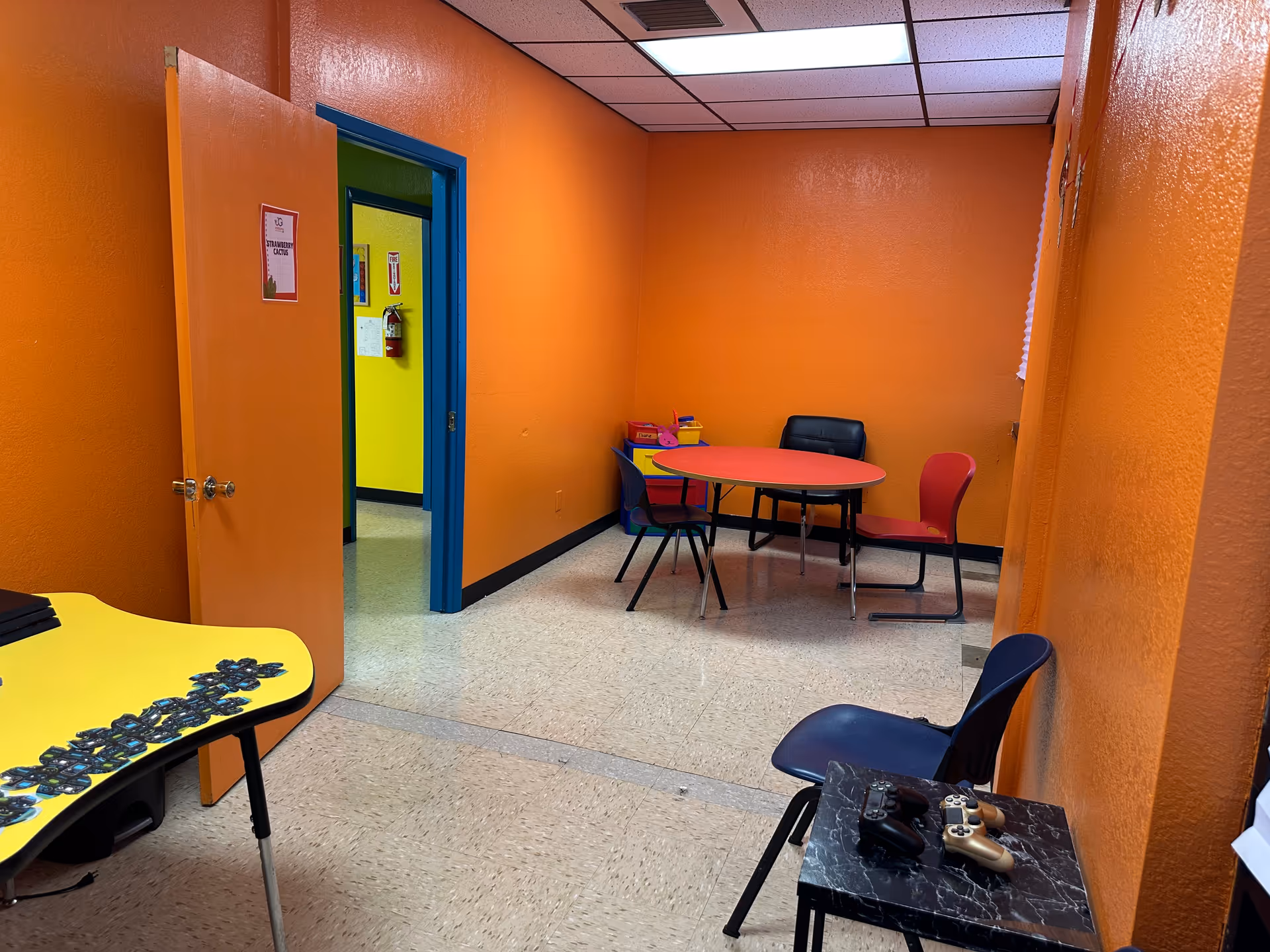 Colorful interior room with orange walls, a round table, chairs, and game controllers.