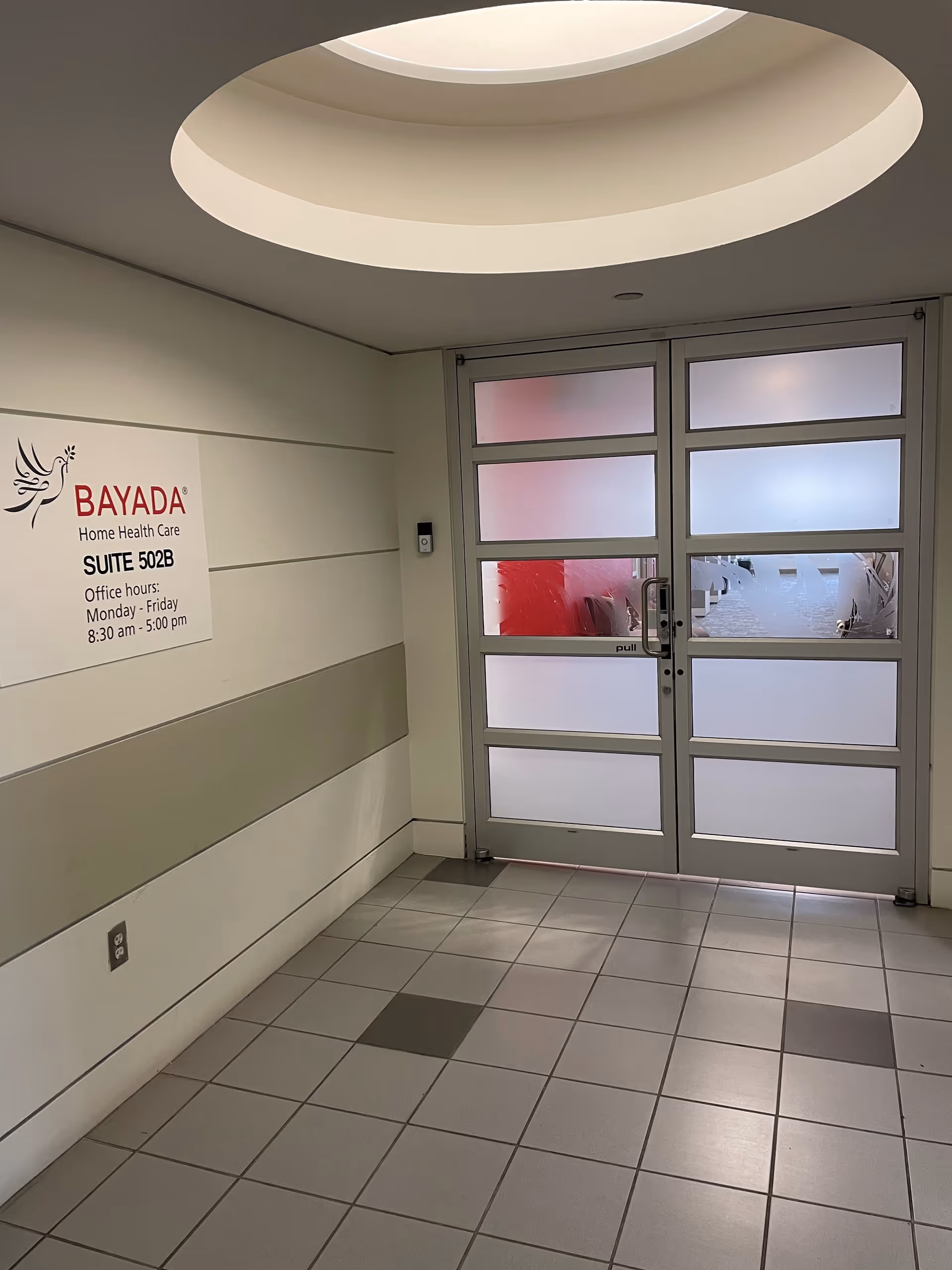 Circular skylight above a white-walled hallway with frosted glass doors and a BAYADA sign.
