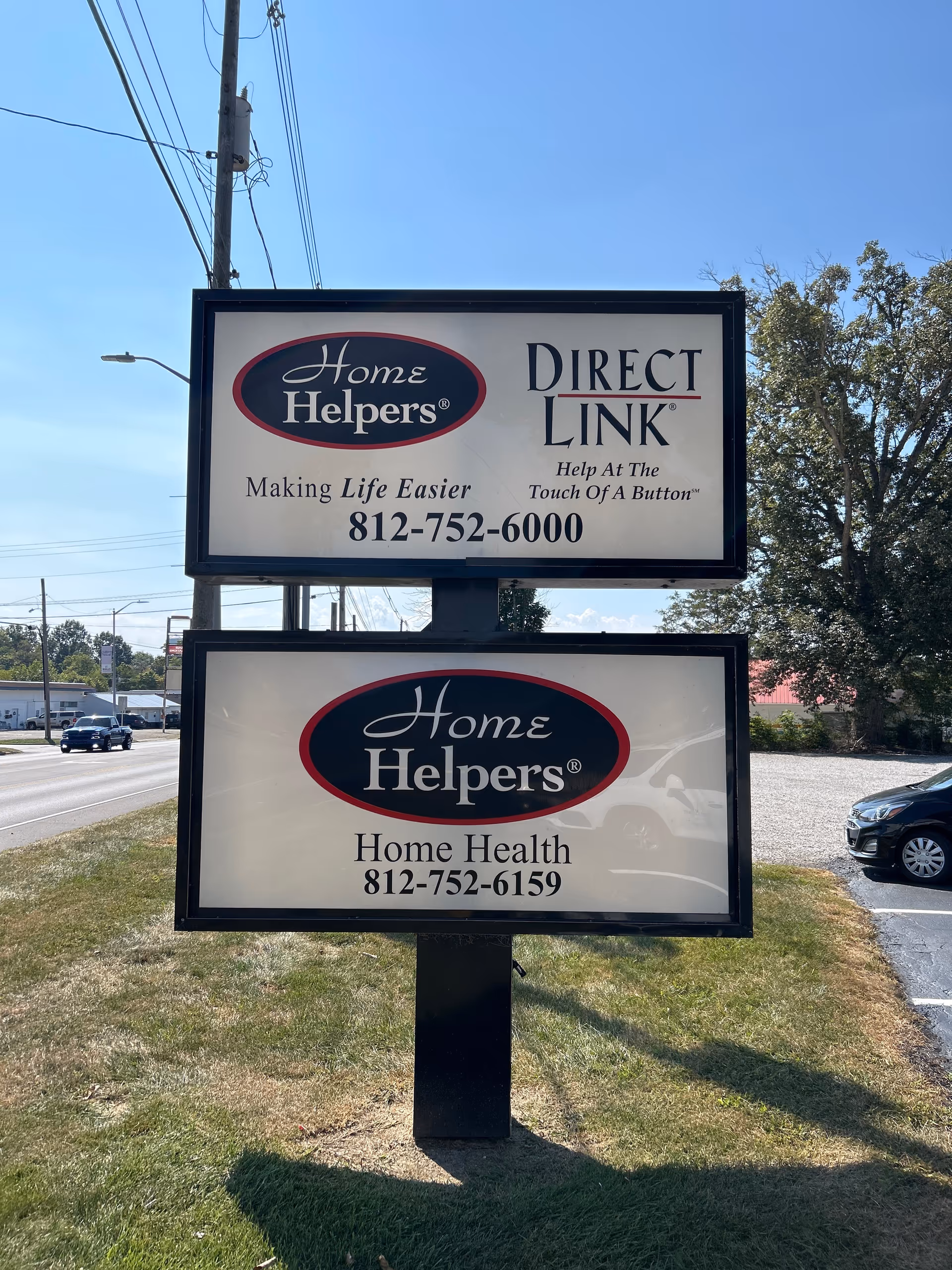 Outdoor sign displays Home Helpers and Direct Link branding beside a road.