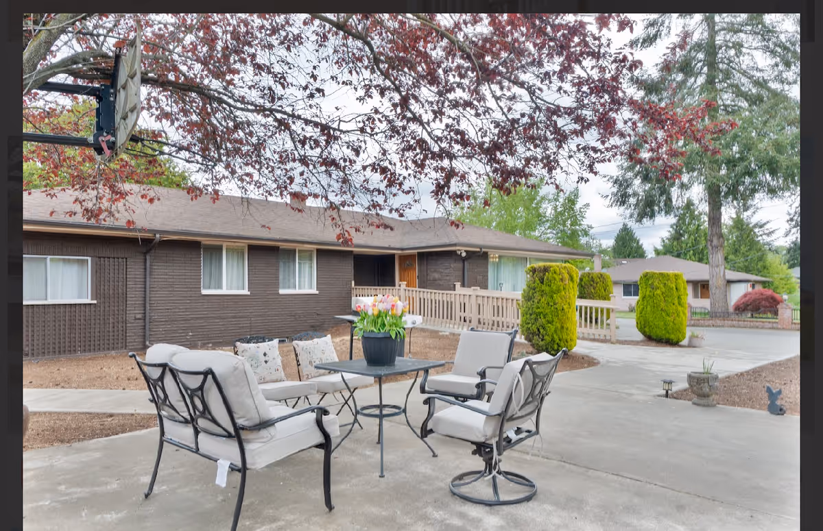 Outdoor patio seating in front of a single-story senior home surrounded by trees.