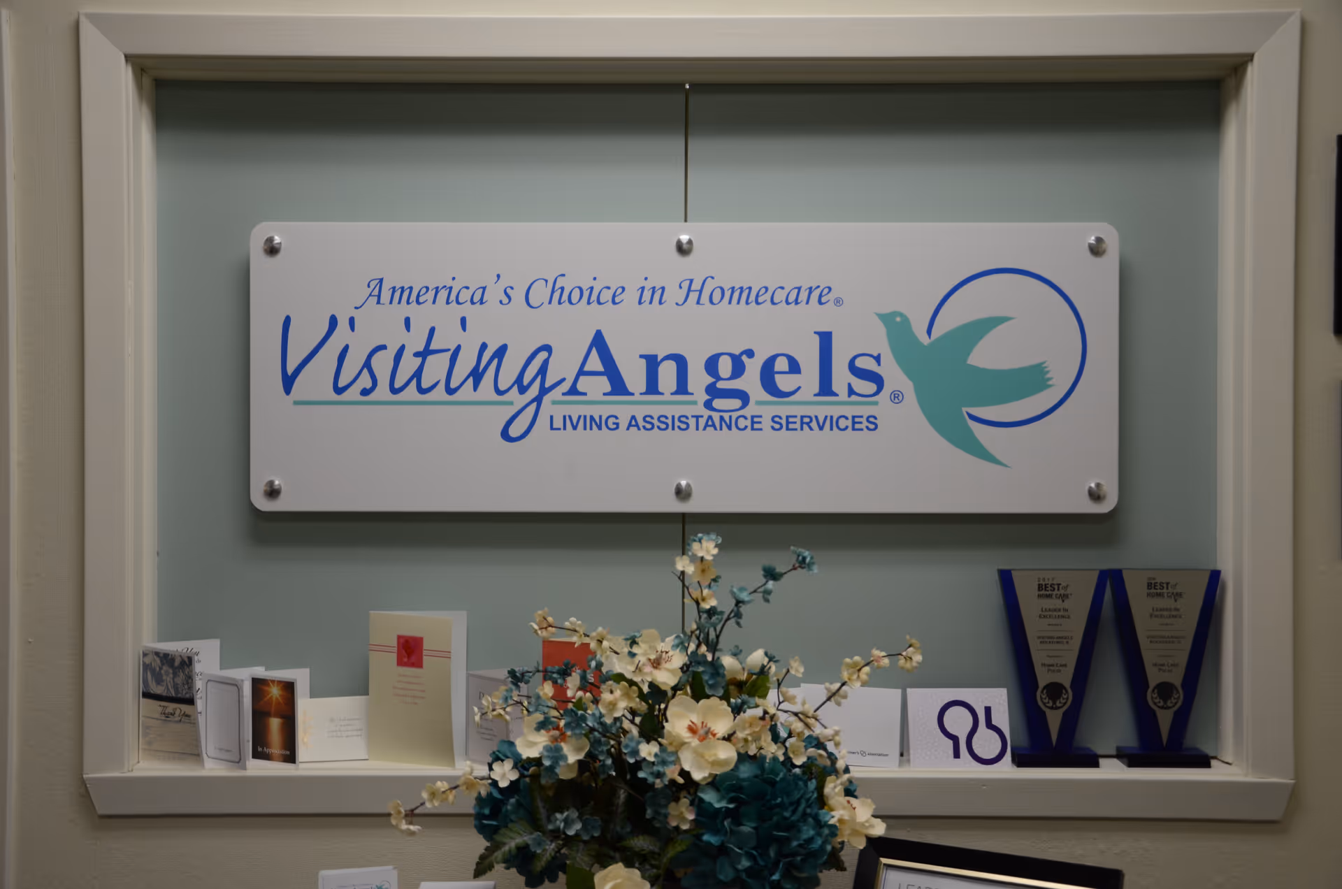 Interior wall with Visiting Angels sign, flower arrangement, and awards display.
