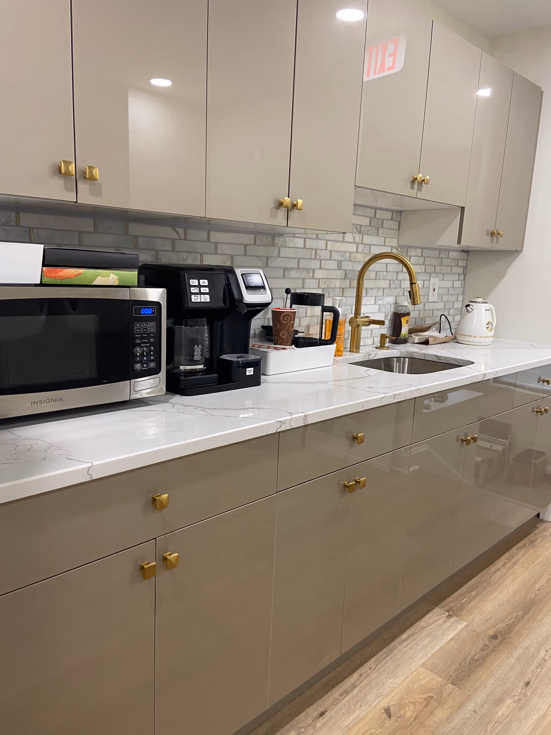 Modern kitchen with gray cabinets, marble countertop, and gold faucet.