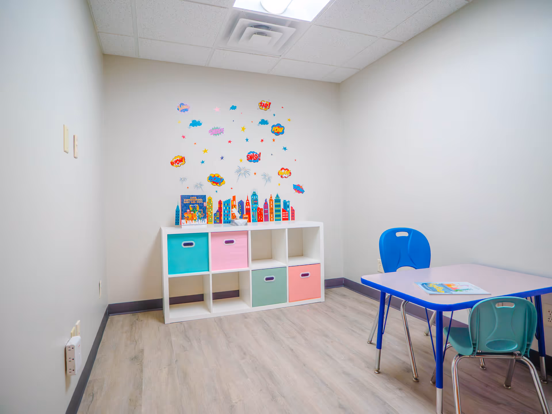 Colorful children's play area with storage cubbies, a small table, pastel chairs, and wall decals.