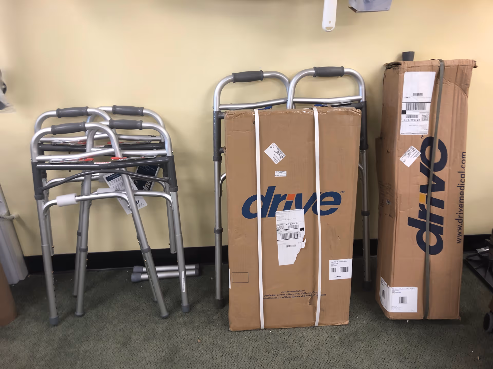 Corner storage area with folded walkers and large boxes against a pale wall.