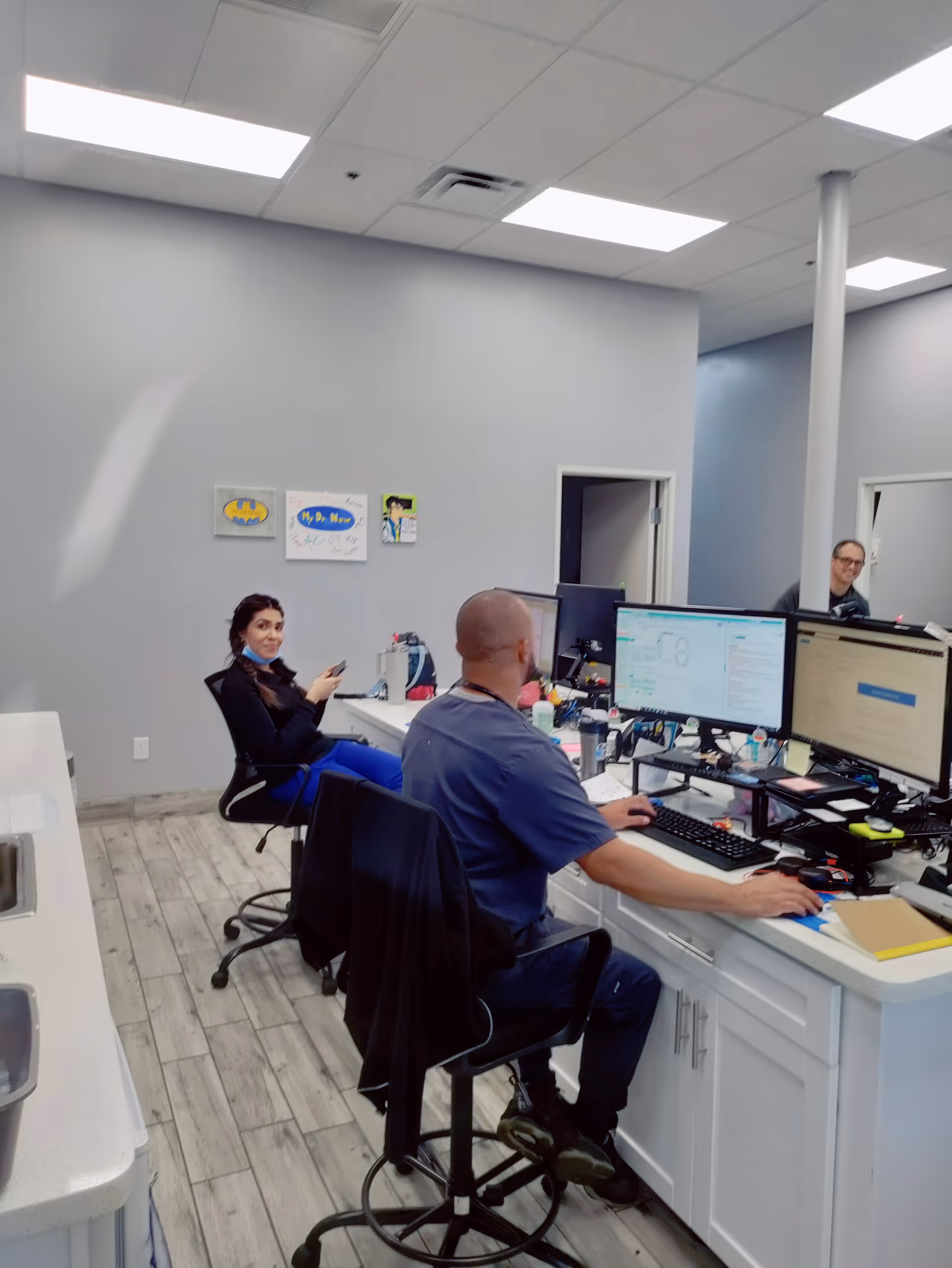 Medical reception area with staff at desks and multiple computer monitors in a bright clinic.