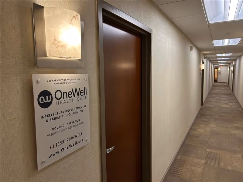 A hallway inside a senior care facility with a door and OneWell Health Care sign.
