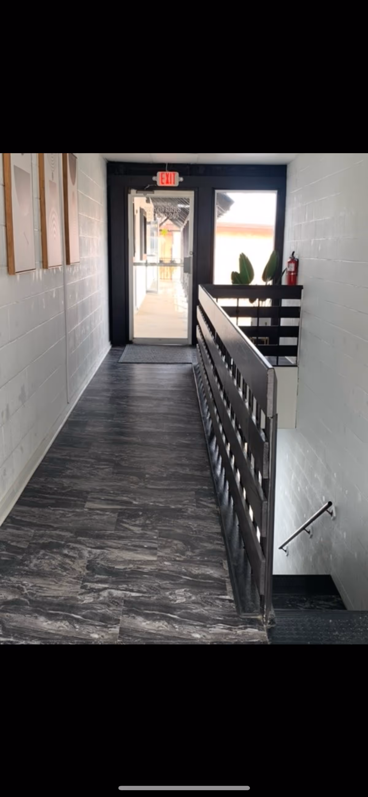Narrow interior hallway with railing, stairs, and an exit door at the end.
