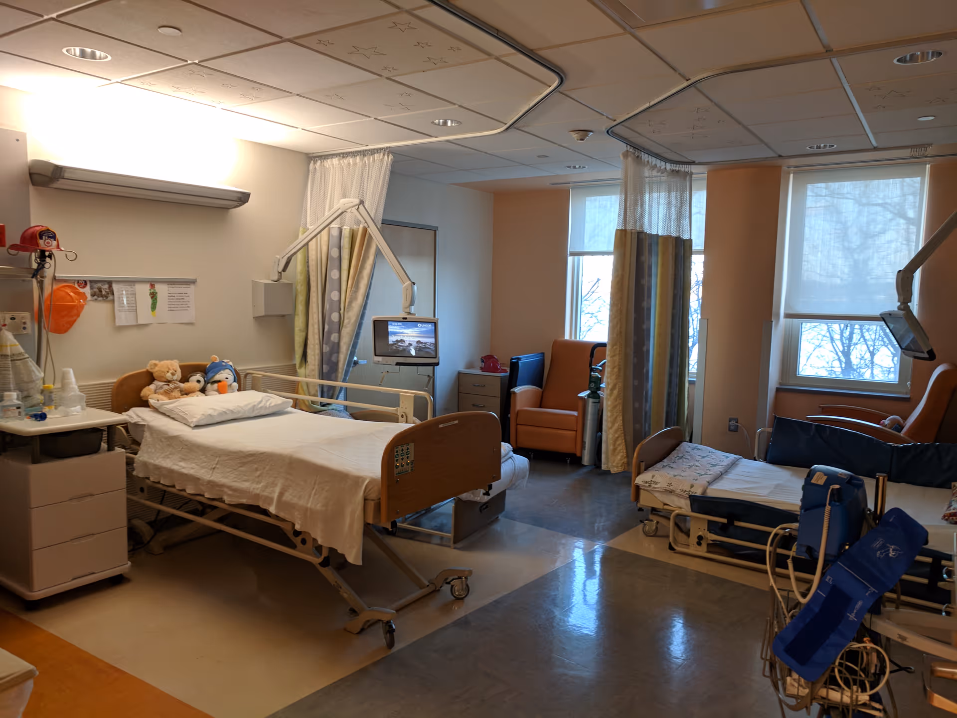 Hospital patient room with bed, curtains, medical equipment, and seating.