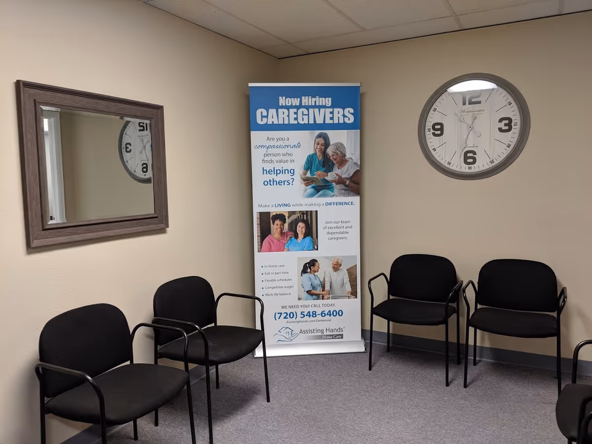 Waiting area inside Assisting Hands Home Care with chairs, a poster banner, clock, and mirror.