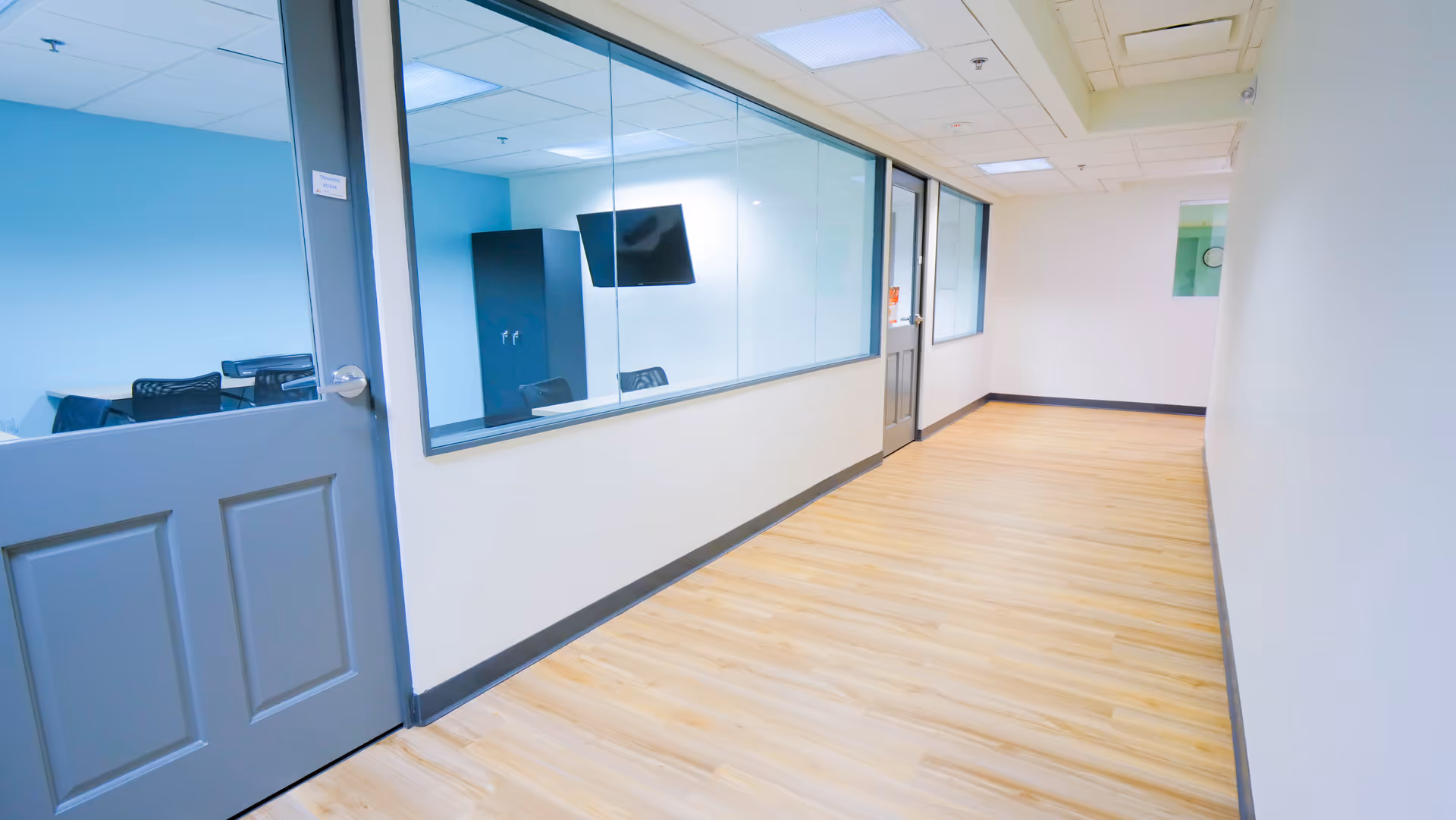 Long interior hallway with glass-walled offices and light wood flooring.