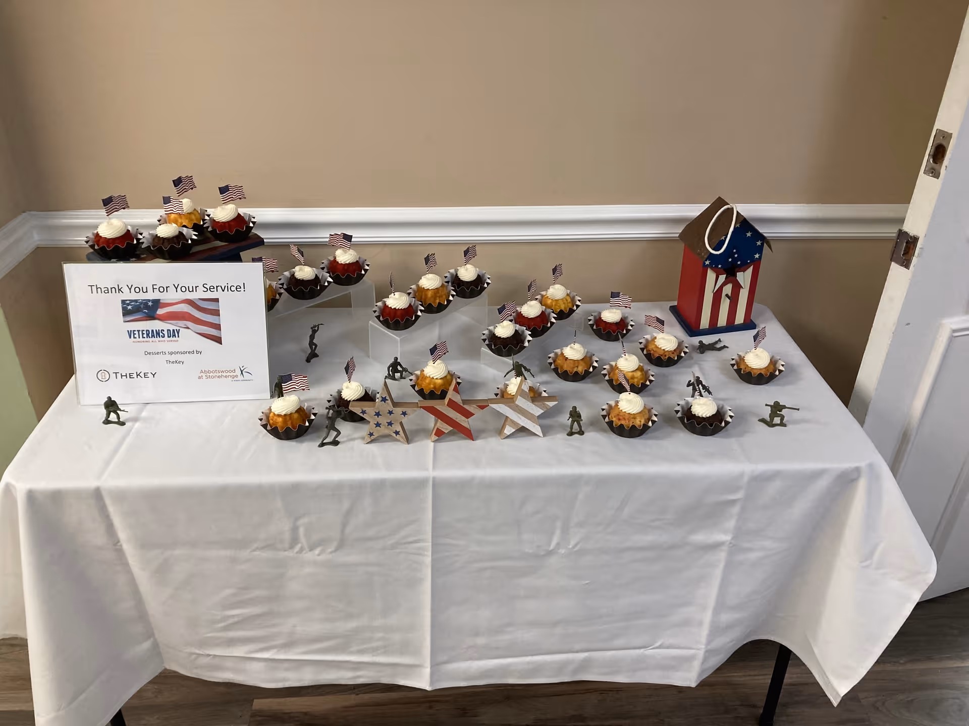 Table of patriotic cupcakes with American flags and a Veterans Day sign indoors.