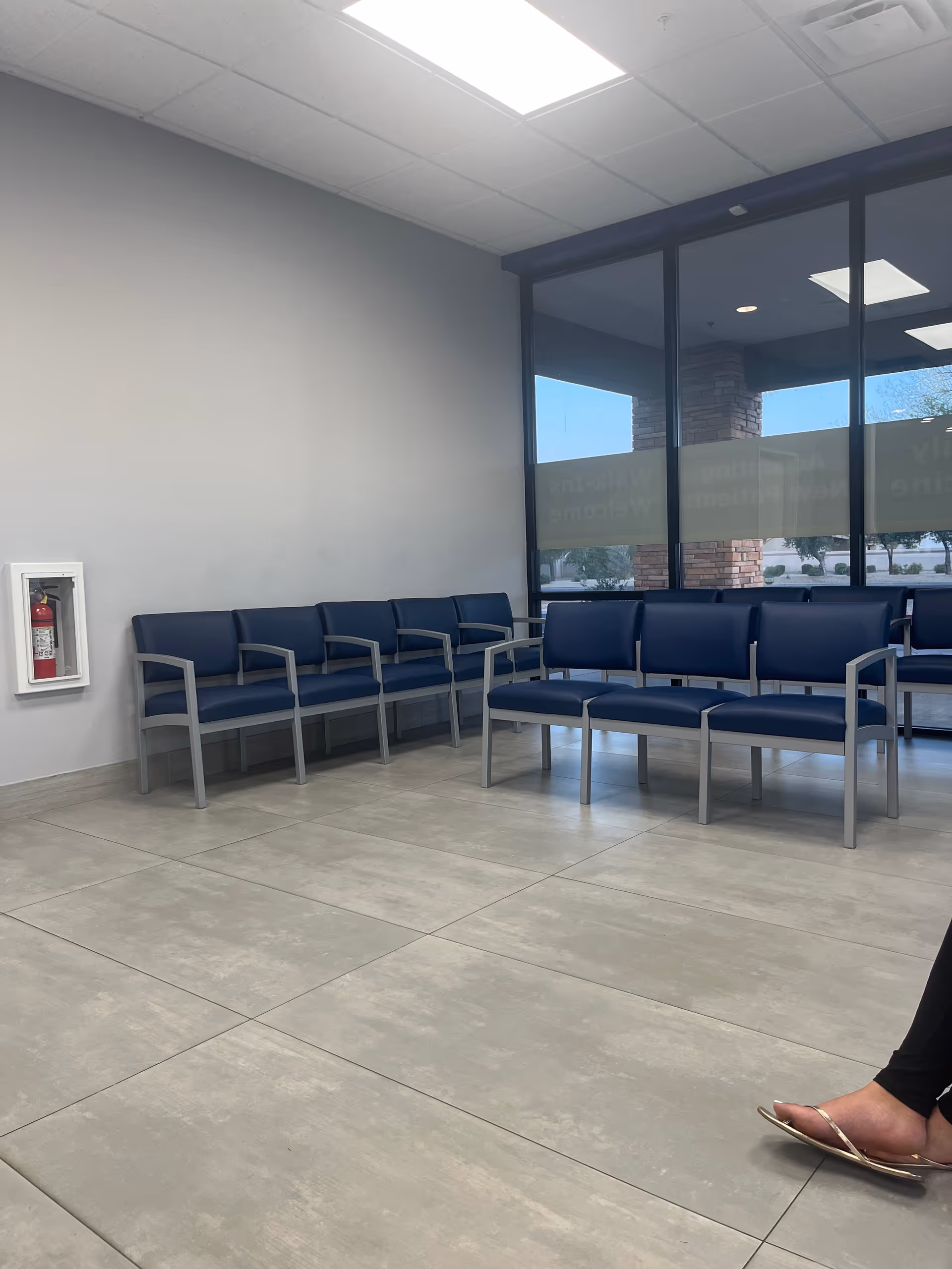 Waiting area with blue chairs along glass windows inside a facility.