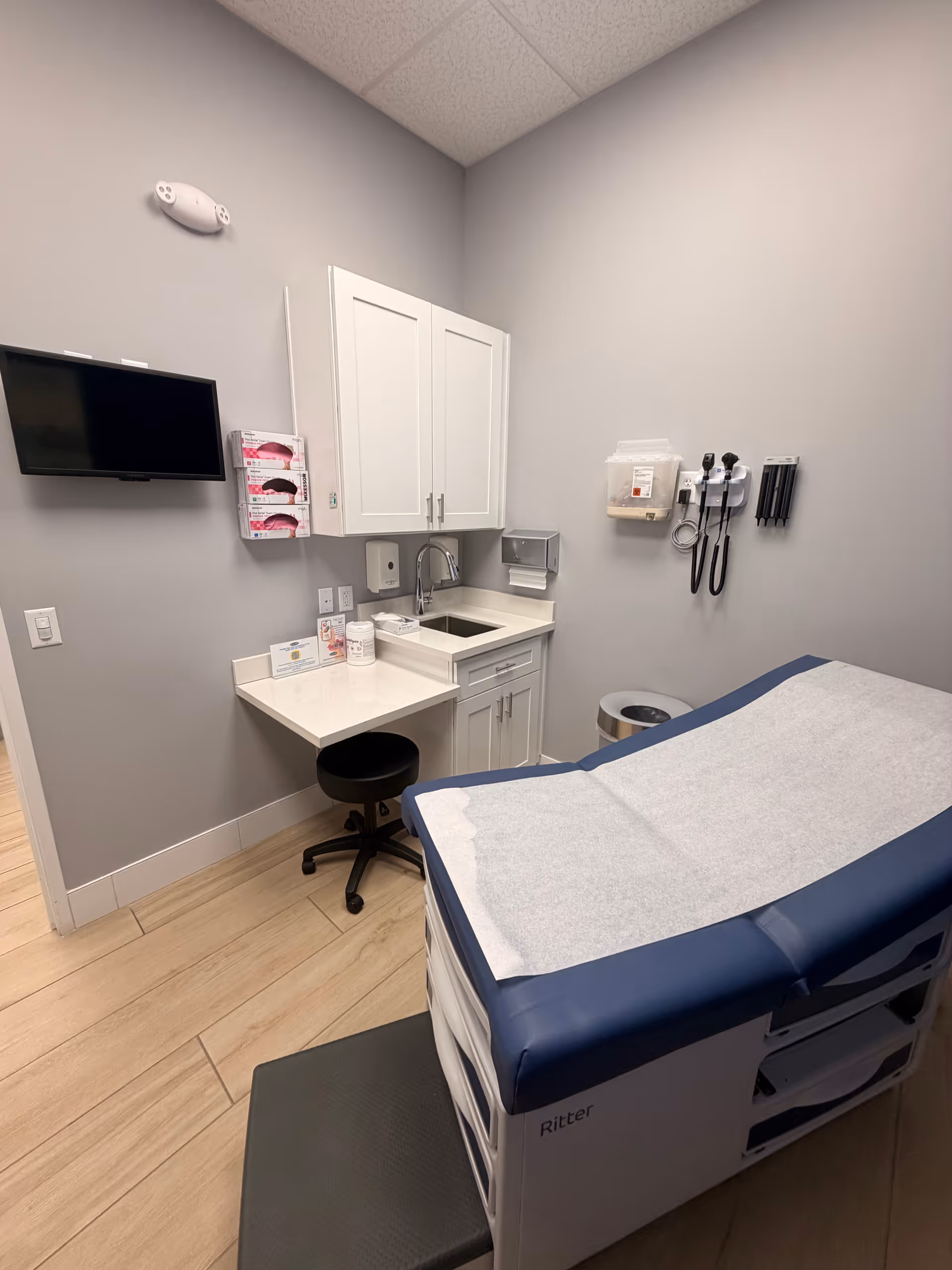Clinical examination room with a hospital bed, sink, cabinets, and medical equipment.