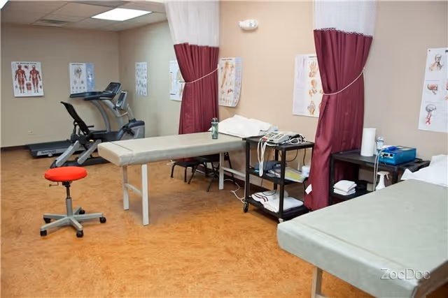 Interior medical treatment room with exam tables, privacy curtains, treadmill, and medical charts.