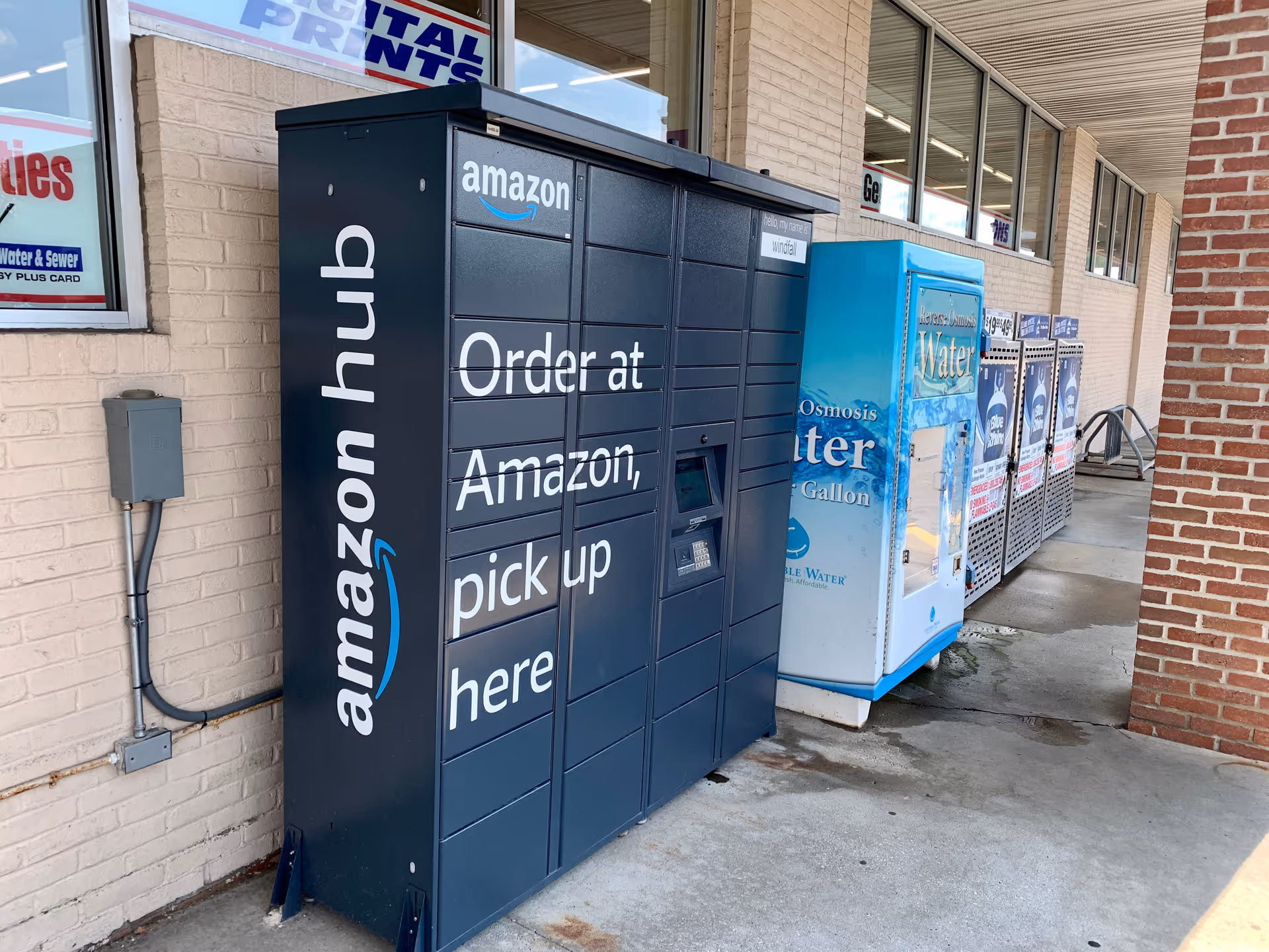 Exterior view of an Amazon Hub locker and water vending machines outside Discount Drug Mart