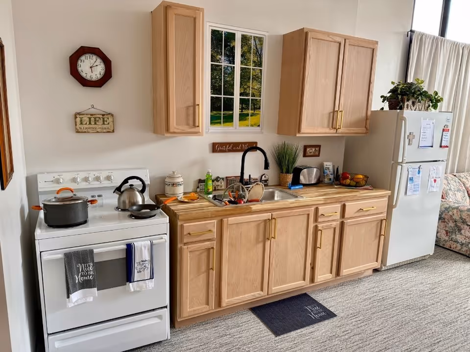 Compact kitchen area with stove, sink, wooden cabinets, and a refrigerator.