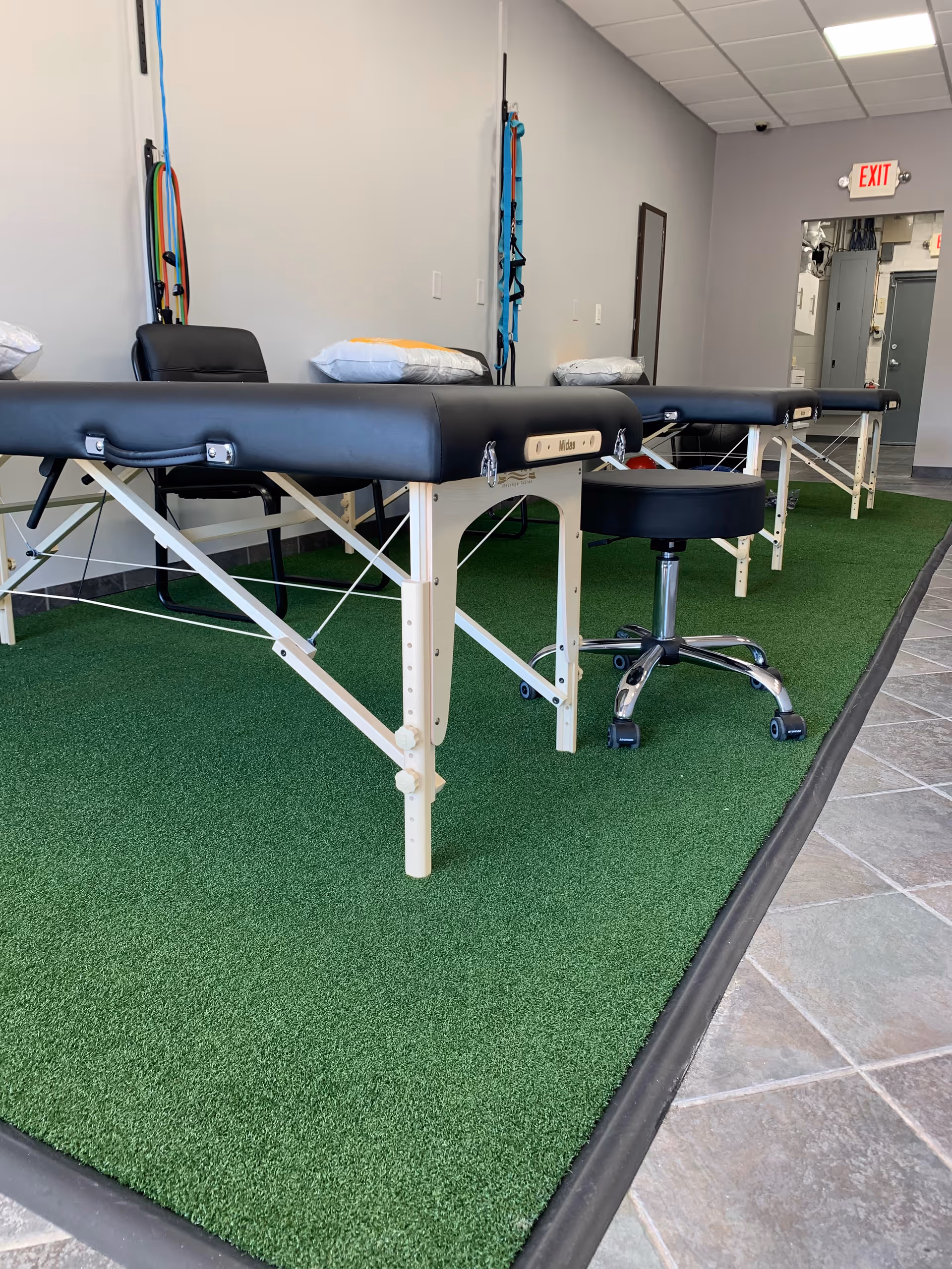 Row of black therapy tables on green carpet in a clinical physical therapy room.