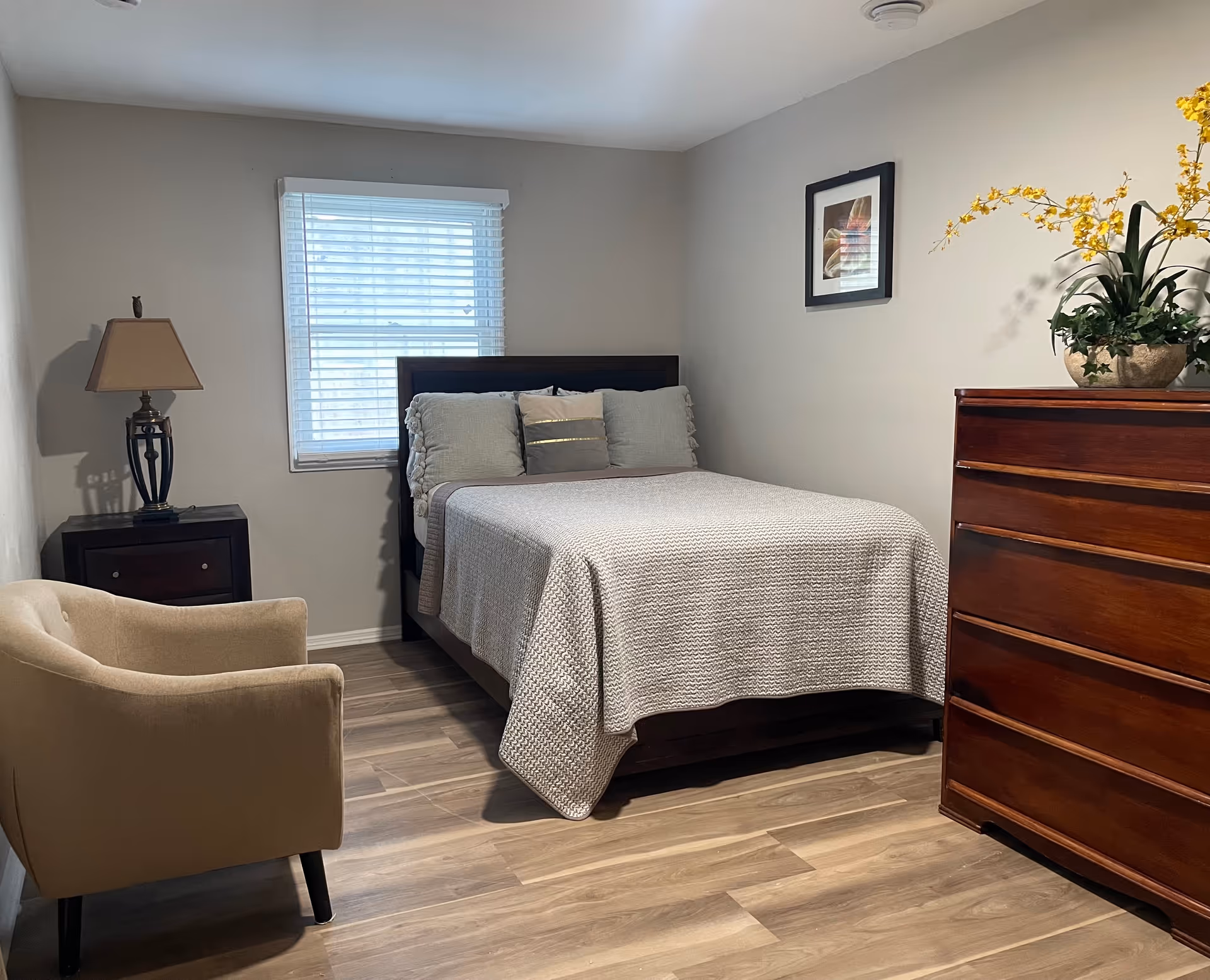 A tidy bedroom with a bed, nightstand, dresser, chair, and window.