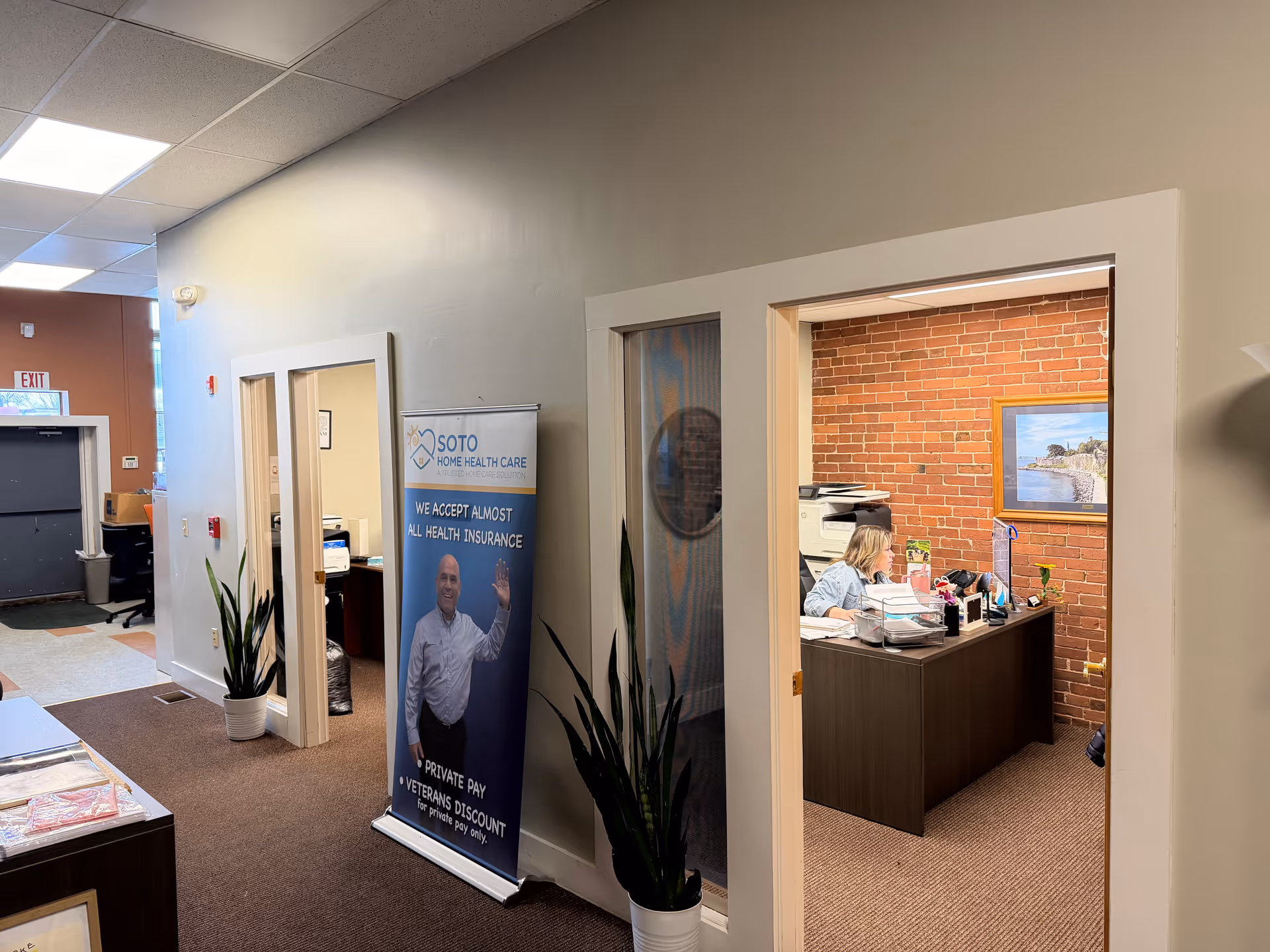 Wide interior hallway at Soto Home Care with a reception desk and brick office wall.