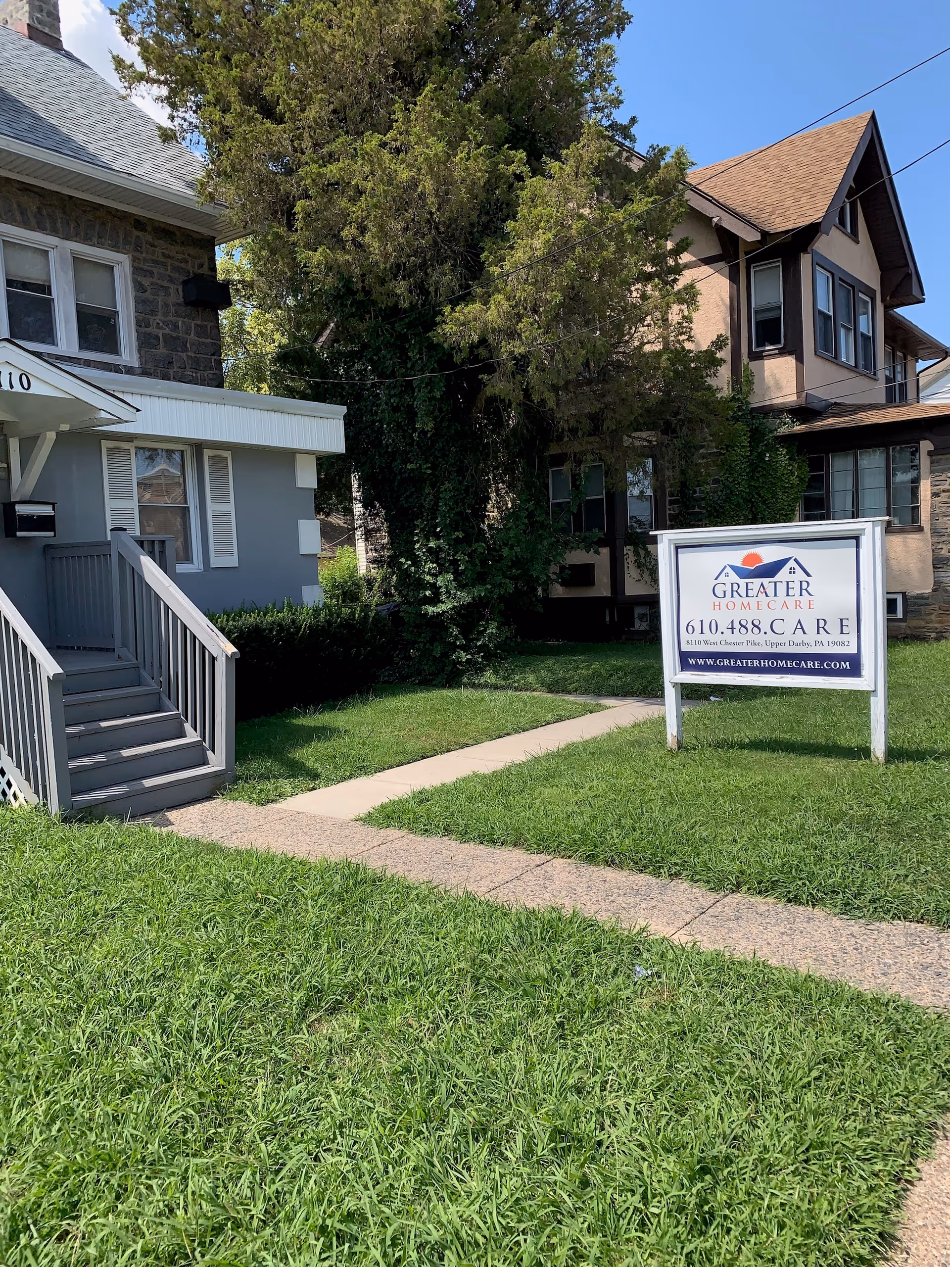 Front view of a residential building with a lawn, sidewalk, and a Greater Homecare sign.