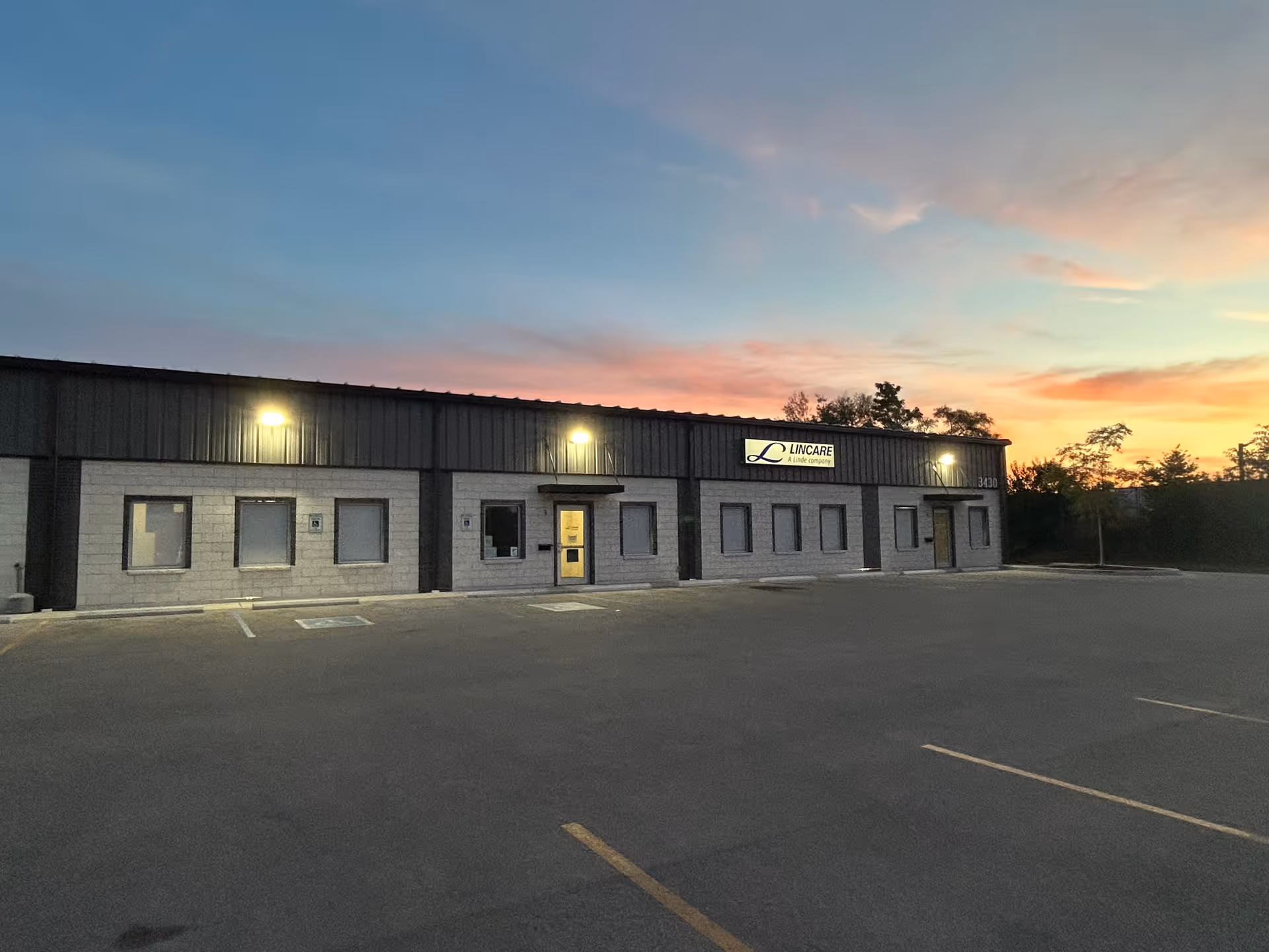 Exterior view of a LINCARE facility with a parking lot and sunset sky.