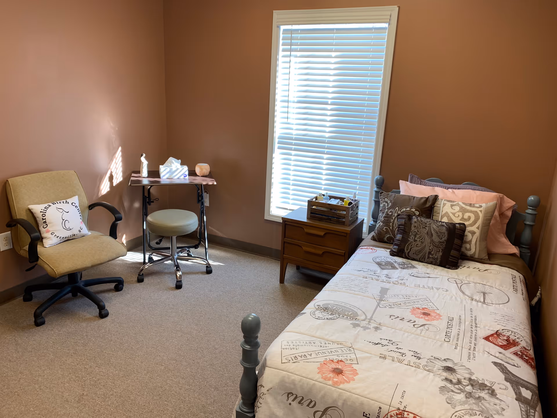 A small pink-walled bedroom with a bed, desk, chair, and window blinds.