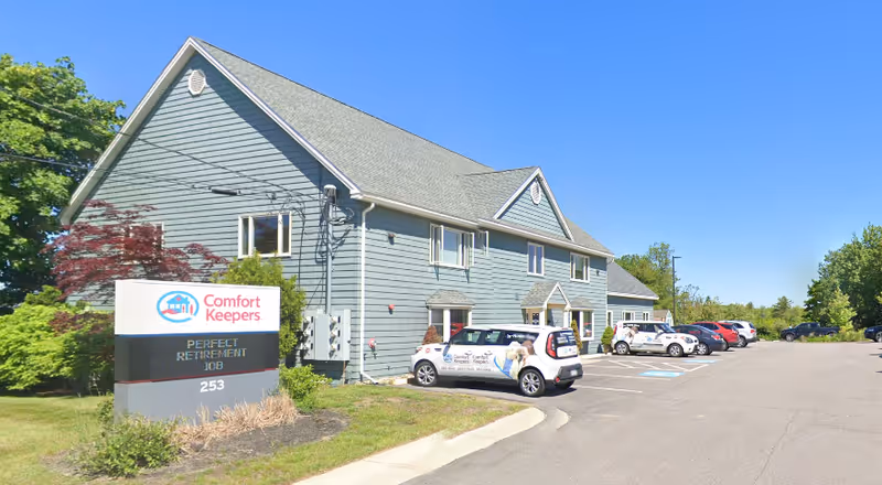 Blue-gray two-story senior care building with parked cars and a Comfort Keepers sign.