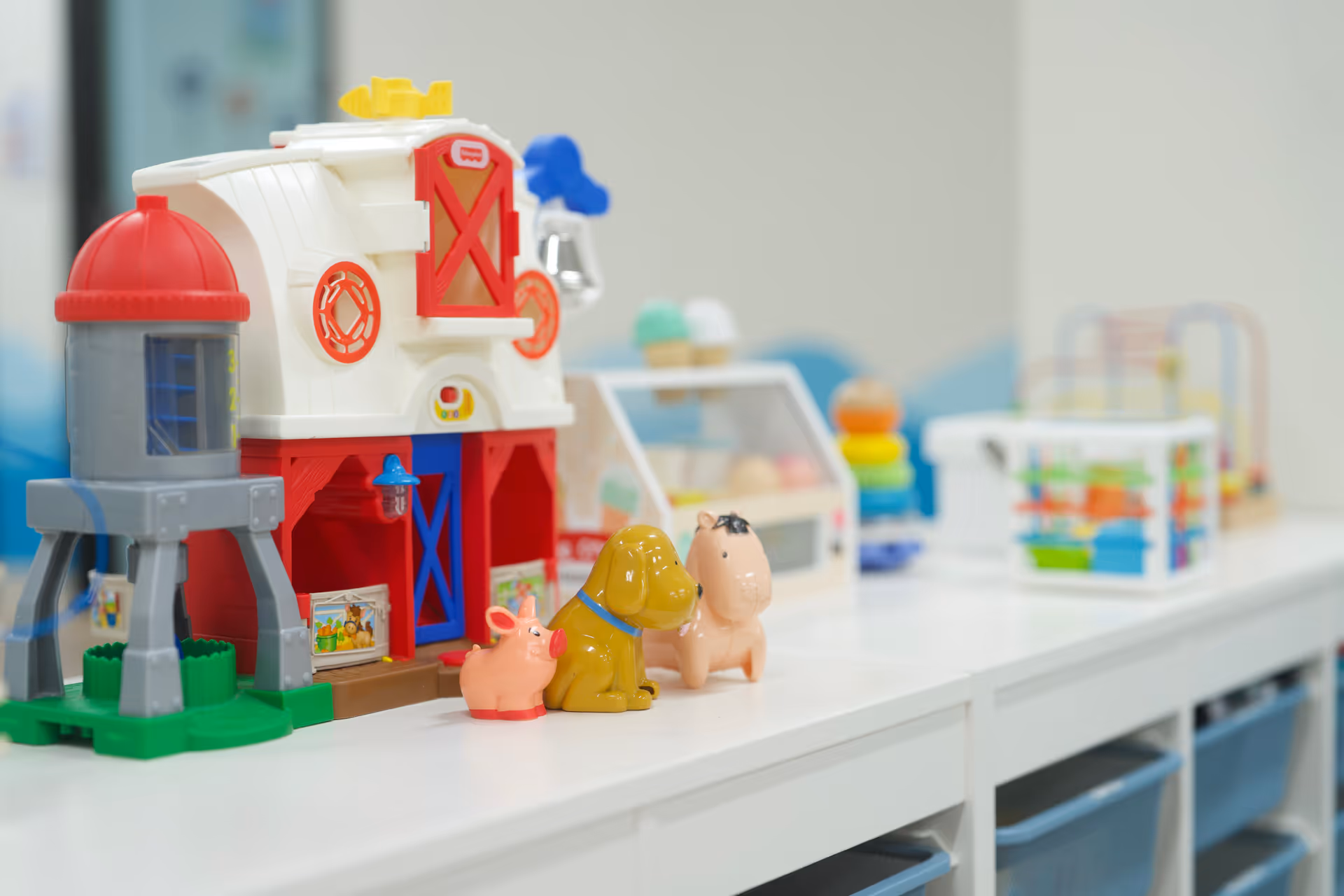 Colorful toy farm playset with animals on a white shelf indoors.